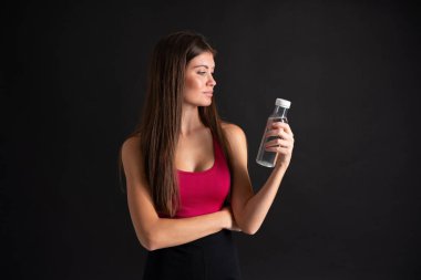 Bir şişe suyla izole edilmiş siyah arka planı olan genç bir kadın.