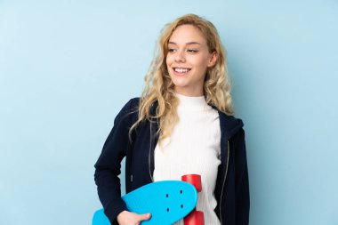 Genç sarışın kadın mavi arka planda tek başına paten kayıyor.