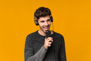 Kulaklıklı ve şarkı söyleyen cep telefonuyla izole edilmiş genç bir adam.