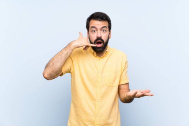 Mavi arka planda sakallı genç bir adam telefon jesti yapıyor ve şüphe ediyor.