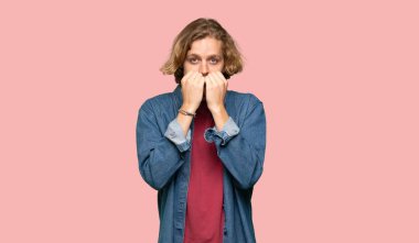 Sarışın adam gergin ve korkmuş renkli arka planda elleri ağıza koyuyor.