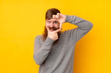 Uzun sakallı, izole edilmiş sarı arka planlı, odaklanmış yüzü olan kızıl saçlı bir adam. Çerçeve sembolü