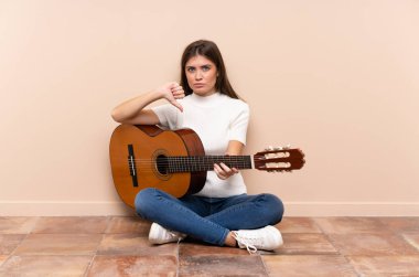 Gitarlı genç bir kadın yere oturmuş, baş parmak işareti gösteriyor.