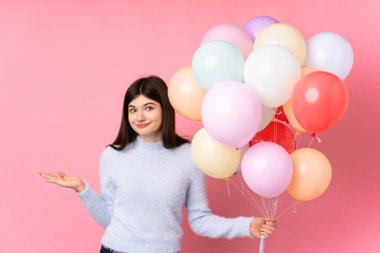 Genç Ukraynalı genç kız pembe arka planda bir sürü balon tutuyor. Kafası karışık bir yüz ifadesi var.