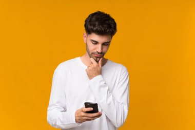 İzole edilmiş turuncu arka plan düşünen ve mesaj gönderen genç bir adam.
