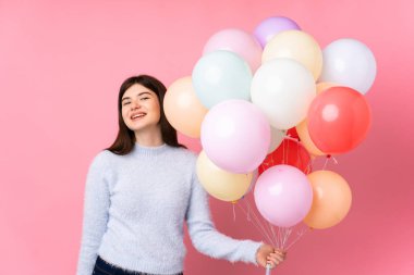 Genç Ukraynalı kız izole edilmiş pembe arka planda bir sürü balon tutuyor ve gülüyor.