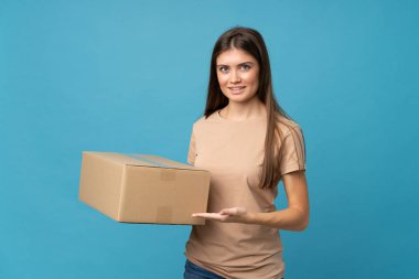 İzole edilmiş mavi arka plan üzerinde genç bir kadın başka bir yere taşımak için bir kutu tutuyor.