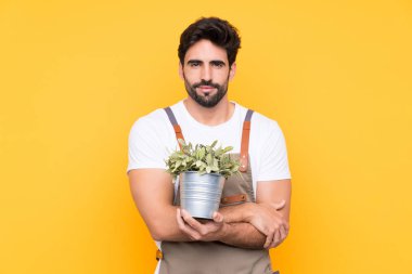 Sarı arka planda sakallı bahçıvan kollarını kavuşturuyor.