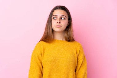 Sarı kazaklı genç bir kız pembe arka planda şüpheli hareketler yapıyor.