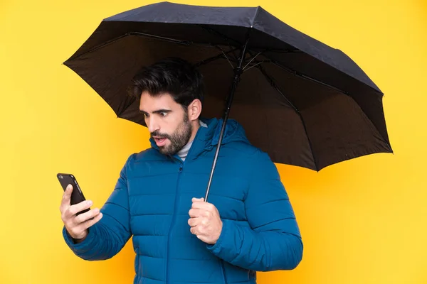Homem segurando um guarda-chuva sobre fundo amarelo isolado — Fotografia de Stock