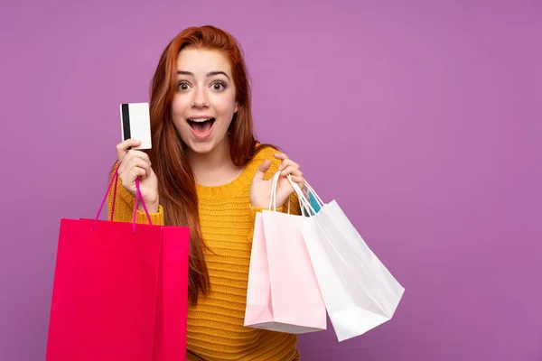 赤毛ティーン女の子上の隔離された紫背景保持ショッピングバッグと驚き — ストック写真