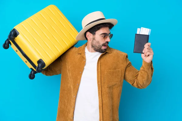 年轻英俊的男人 留着胡子 蓝色背景 带着手提箱和护照 带着惊喜度假 — 图库照片