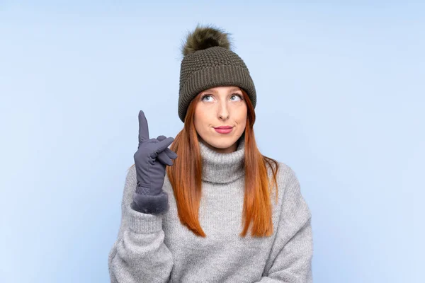 若いですRedheadロシアの女性とともに冬の帽子以上隔離された青の背景指していますザインデックス指A素晴らしいアイデア — ストック写真