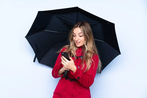 Mujer joven con abrigo de invierno sosteniendo un paraguas y un móvil — Foto de Stock