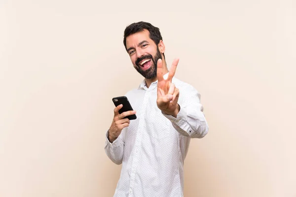 Joven Con Barba Sosteniendo Móvil Sonriendo Mostrando Señal Victoria —  Fotos de Stock