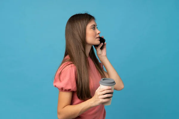Giovane Donna Sfondo Blu Isolato Possesso Caffè Portare Cellulare — Foto Stock