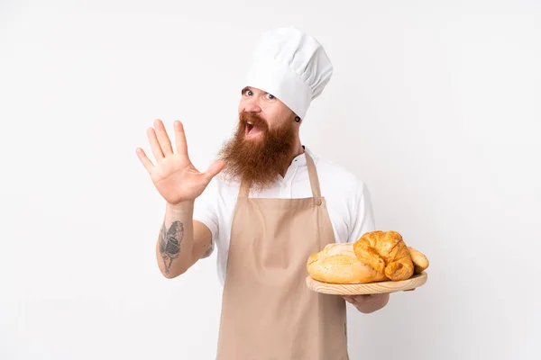 シェフの制服を着た赤毛の男 幸せな表情で手で塩焼きいくつかのパンとテーブルを保持男性パン屋 — ストック写真