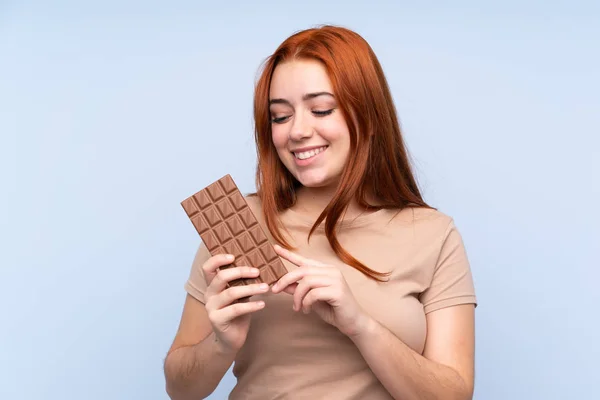 Redhead Teenager Dívka Přes Izolované Modré Pozadí Čokoládovou Tabletu Šťastný — Stock fotografie