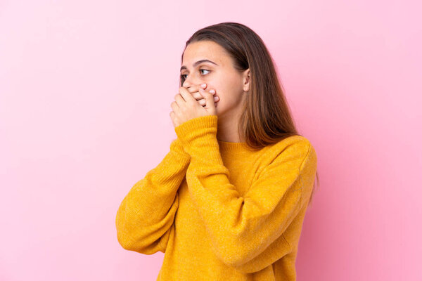 Teenager girl with yellow sweater over isolated pink background covering mouth and looking to the side