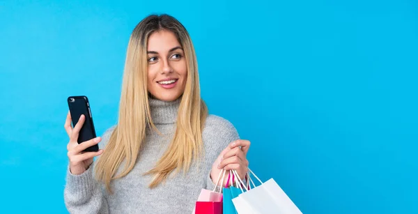 Ung Uruguayansk Kvinna Över Isolerad Blå Bakgrund Håller Shoppingväskor Och — Stockfoto