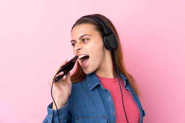 Teenager κορίτσι ακούγοντας μουσική με ένα κινητό πάνω από απομονωμένο ροζ w — Φωτογραφία Αρχείου