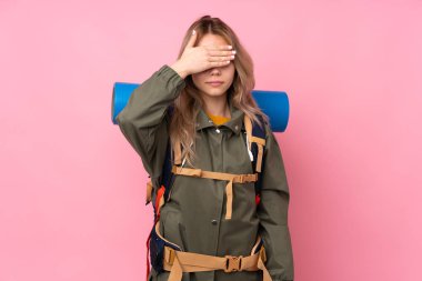 Genç Rus dağcı kız büyük bir sırt çantası ile pembe arka planda izole edilmiş gözlerini elleriyle kapatıyor. Bir şey görmek istemiyorum.