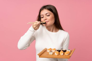 Soyutlanmış pembe arka planda suşi yiyen genç bir kız.