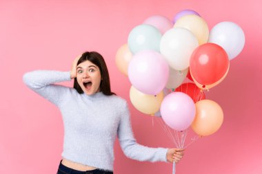 Genç Ukraynalı genç kız, pembe arka planda bir sürü balon tutuyor ve sürpriz bir yüz ifadesi var.
