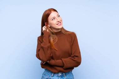 Genç kızıl saçlı kadın, izole edilmiş mavi arka planda bir fikir düşünüyor.