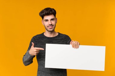 İzole edilmiş arka planı olan genç bir adam bir konsept eklemek için boş beyaz bir levha tutuyor.