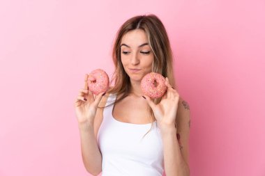 Soyutlanmış pembe arka planda donut tutan genç bir kadın.