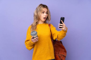 Mor arka planda izole edilmiş genç bir Rus öğrenci. Elinde kahve ve cep telefonu var.