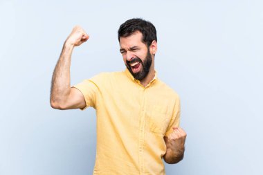 Mavi arka planda sakallı genç bir adam zaferi kutluyor.