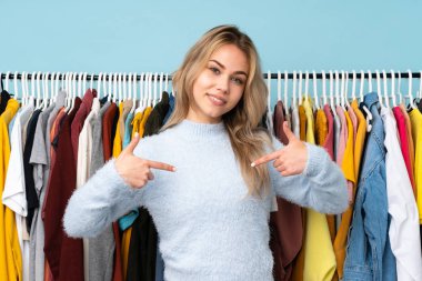 Genç Rus kız mavi arka planda soyutlanmış giysiler alıyor gururlu ve kendini beğenmiş.