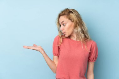 Mavi arka planda izole edilmiş genç sarışın kadın avucunun içinde hayali bir alan tutuyor.