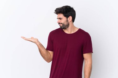 İzole edilmiş beyaz arka planda sakallı yakışıklı bir genç. Kopyalama alanını şüphe ile tutuyor.