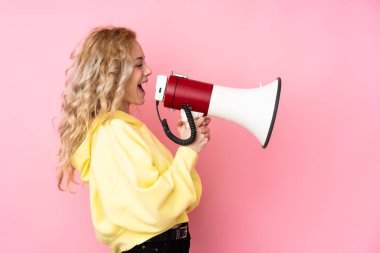 Pembe arka planda izole edilmiş sweatshirt giyen genç sarışın kadın megafondan bağırıyor.