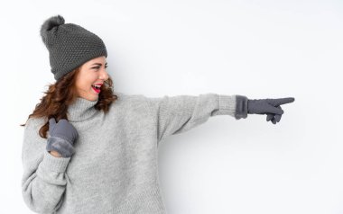 İzole edilmiş beyaz arka planı olan, kışlık şapkalı genç bir Rus kadını işaret ediyor.