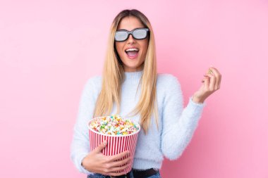 Genç Uruguaylı kadın pembe arka planda 3D gözlüklü ve elinde koca bir kova patlamış mısır tutuyor.