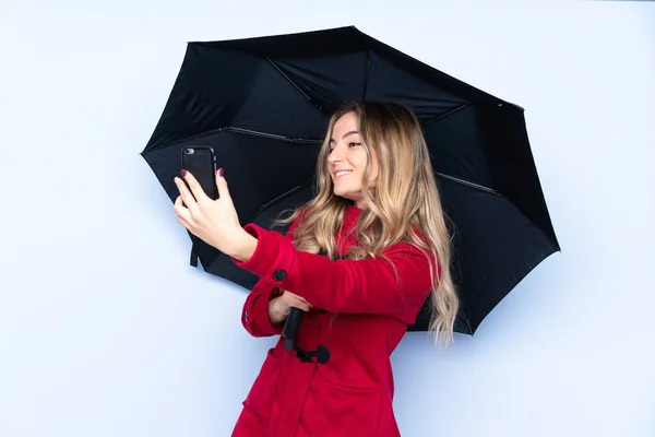 Mujer joven con abrigo de invierno sosteniendo un paraguas y un móvil — Foto de Stock