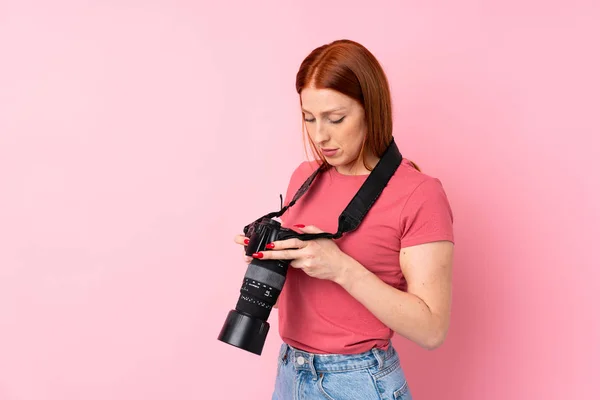 Joven Pelirroja Sobre Fondo Rosa Aislado Con Una Cámara Profesional —  Fotos de Stock