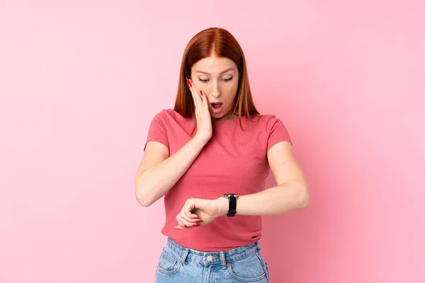 Jovem Ruiva Sobre Fundo Rosa Isolado Com Relógio Pulso Surpreso — Fotografia de Stock