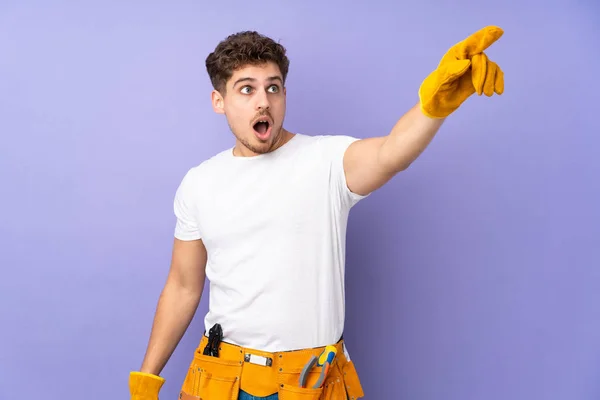 Jovem Eletricista Homem Sobre Isolado Fundo Roxo Apontando Para Longe — Fotografia de Stock