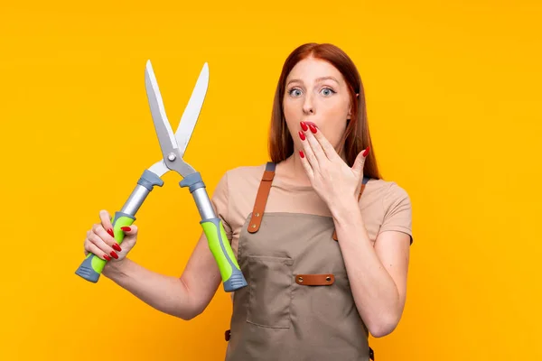 Young redhead gardener woman withpruning shears over isolated yellow background — Stock Photo, Image