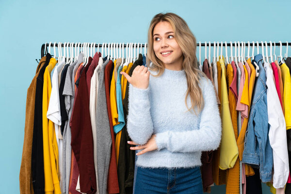 Teenager Russian girl buying some clothes isolated on blue background pointing to the side to present a product