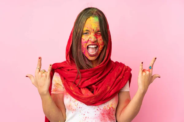 若いですインドの女性とともにカラフルなホリパウダーオン彼女の顔絶縁ピンクの背景作りホーンジェスチャー — ストック写真