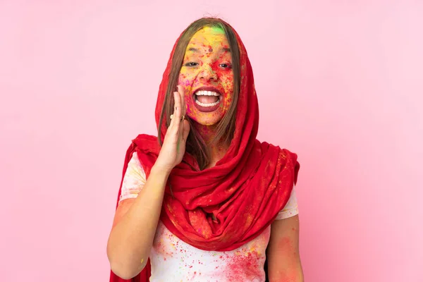 Young Indian woman with colorful holi powders on her face isolated on pink background shouting with mouth wide open