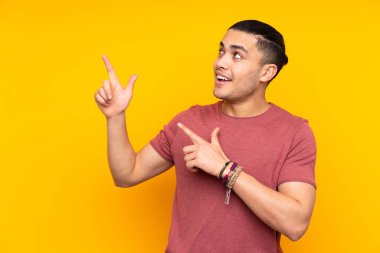 Asyalı yakışıklı adam, sarı arka planda izole edilmiş. Yan tarafı işaret ediyor ve sessiz hareketler yapıyor.
