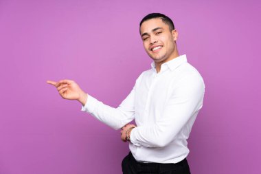 Asyalı yakışıklı adam mavi arka planda izole edilmiş, parmağını yana doğru gösteriyor.