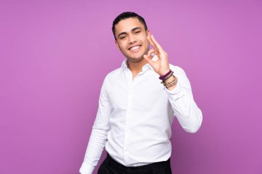 Asyalı yakışıklı adam mavi arka planda izole edilmiş. Parmaklarıyla işaret veriyor.